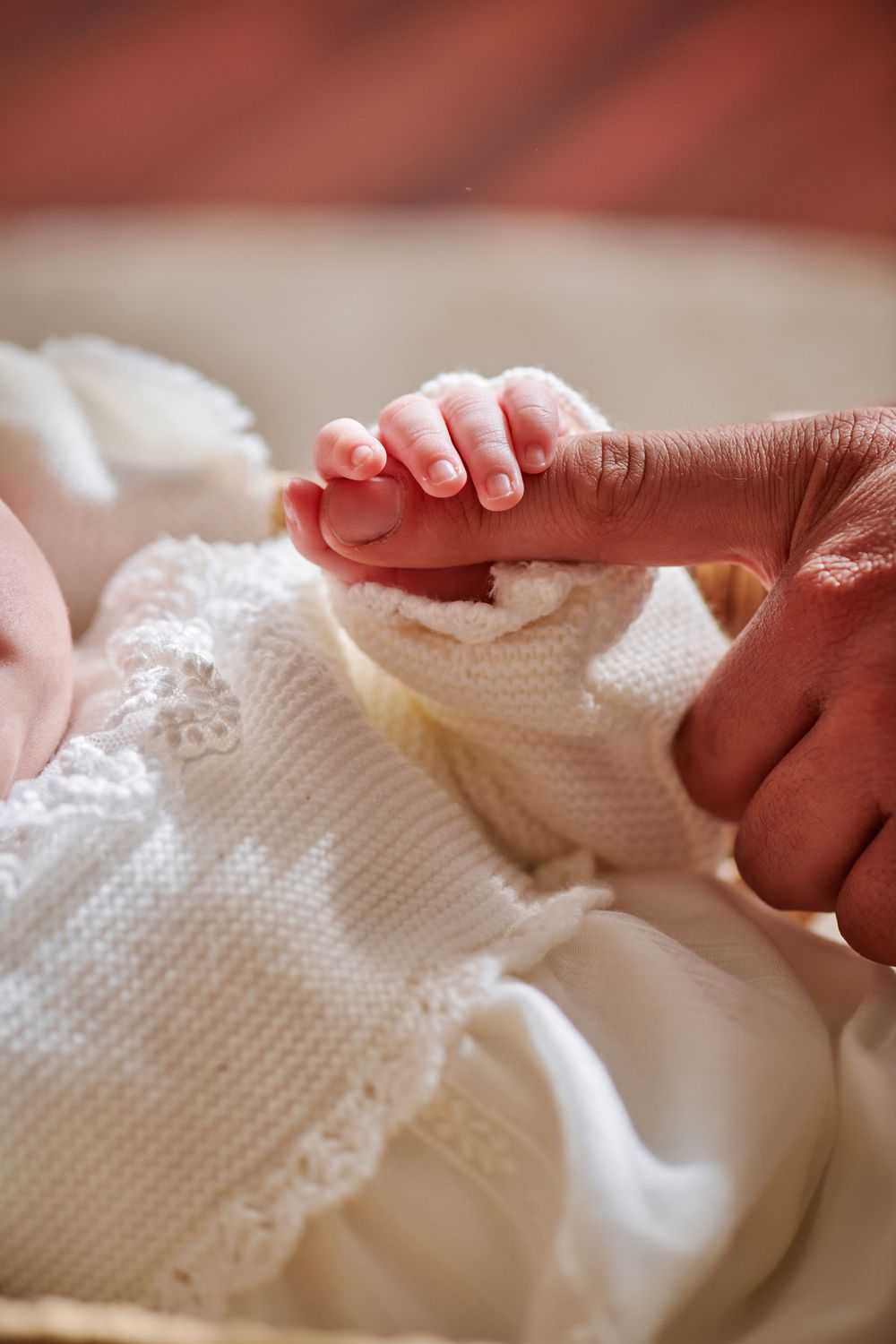 Close-up of a newborn baby grasping an adult's finger, wrapped in a white knit blanket.