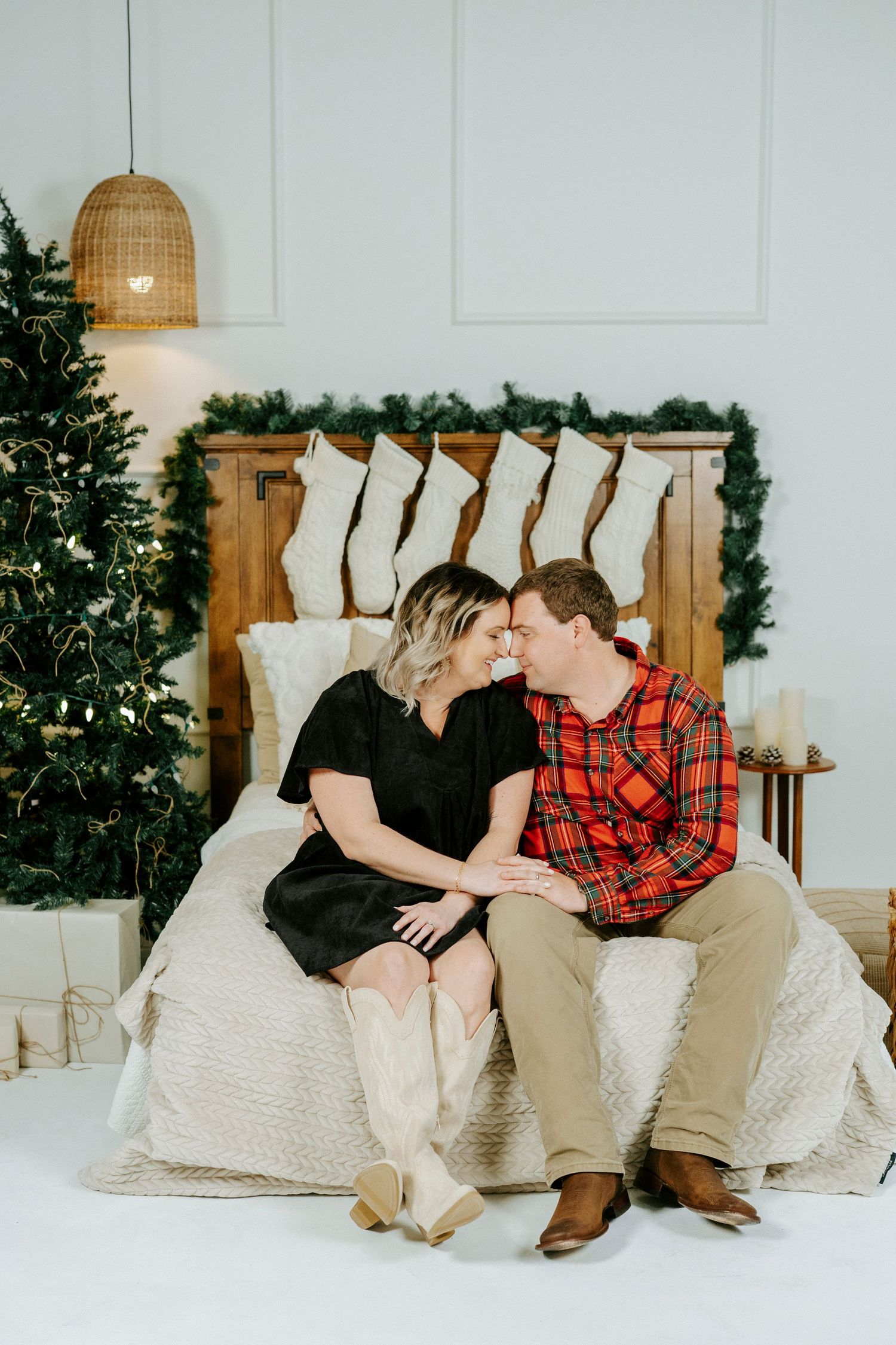 A couple sitting on a white couch shares intimate moments in a holiday setting with Christmas decor in the background.