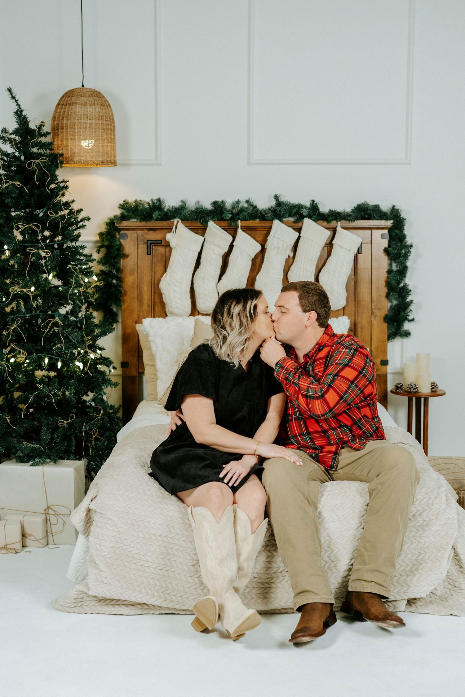 Romantic holiday scene with couple sitting on couch by Christmas tree and white decor in cozy living room setting.