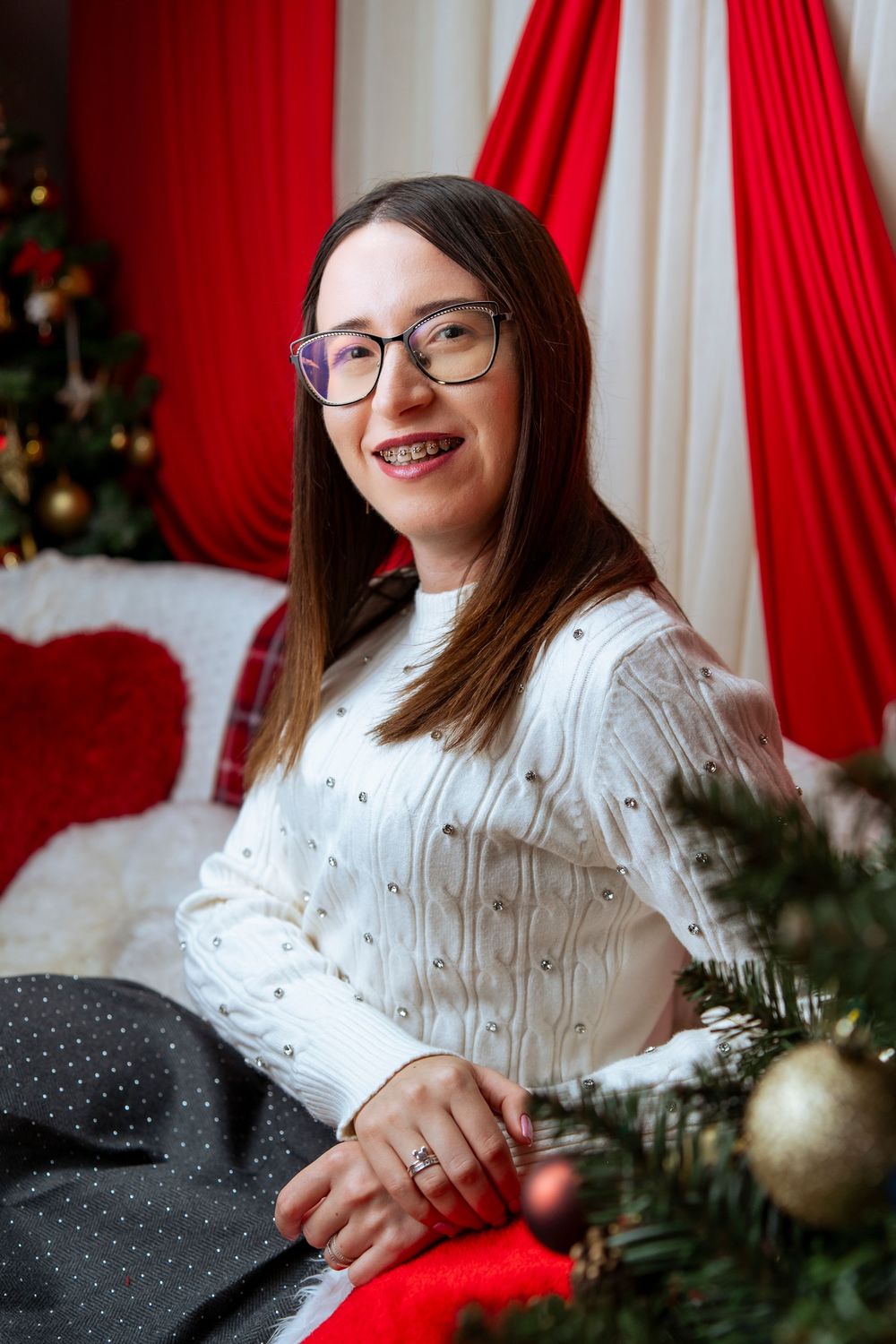 A festive holiday portrait series showing someone in a white sweater against red curtains and Christmas decorations.