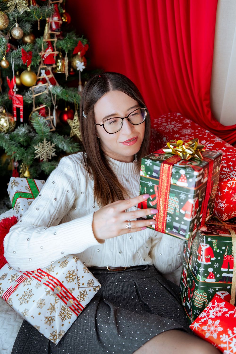 Festive holiday scene with wrapped presents and Christmas tree decorations against a red backdrop.
