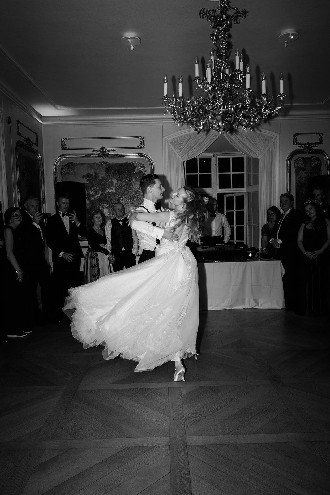 A black and white wedding photograph showing a couple in formal attire standing together in an elegant indoor setting.