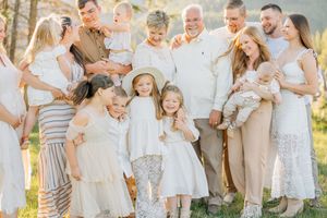 A large family group wearing coordinated white and neutral outfits gathers outdoors for a casual portrait session.