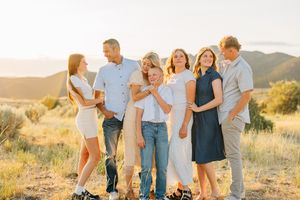 A group gathers on a grassy hillside during golden hour with mountains in the background.