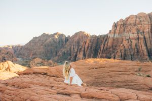 Dramatic red rock cliffs and desert landscape at sunset with figure in white dress.