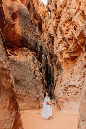 A person in a flowing dress explores a narrow slot canyon with towering sandstone walls.