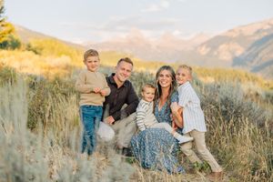 Family plays together in tall grass with mountain landscape in background at sunset.