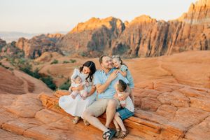 Family relaxes together on red sandstone rocks during desert sunset photo shoot.
