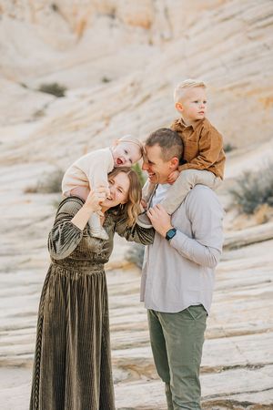 Parents playing with baby on sloping desert rock formations during family photoshoot.