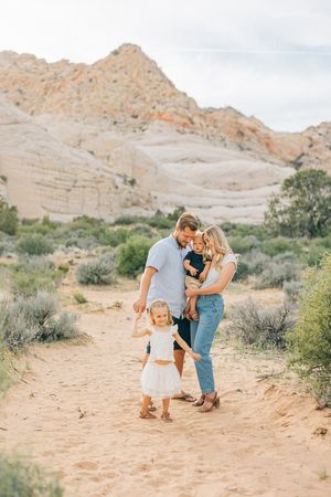 Family walking together through sandy desert terrain surrounded by rock formations.
