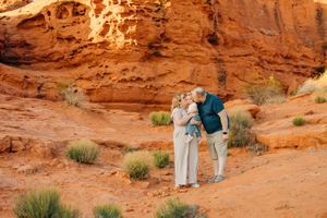 Two people walk together along a winding trail through towering red rock formations in the desert.