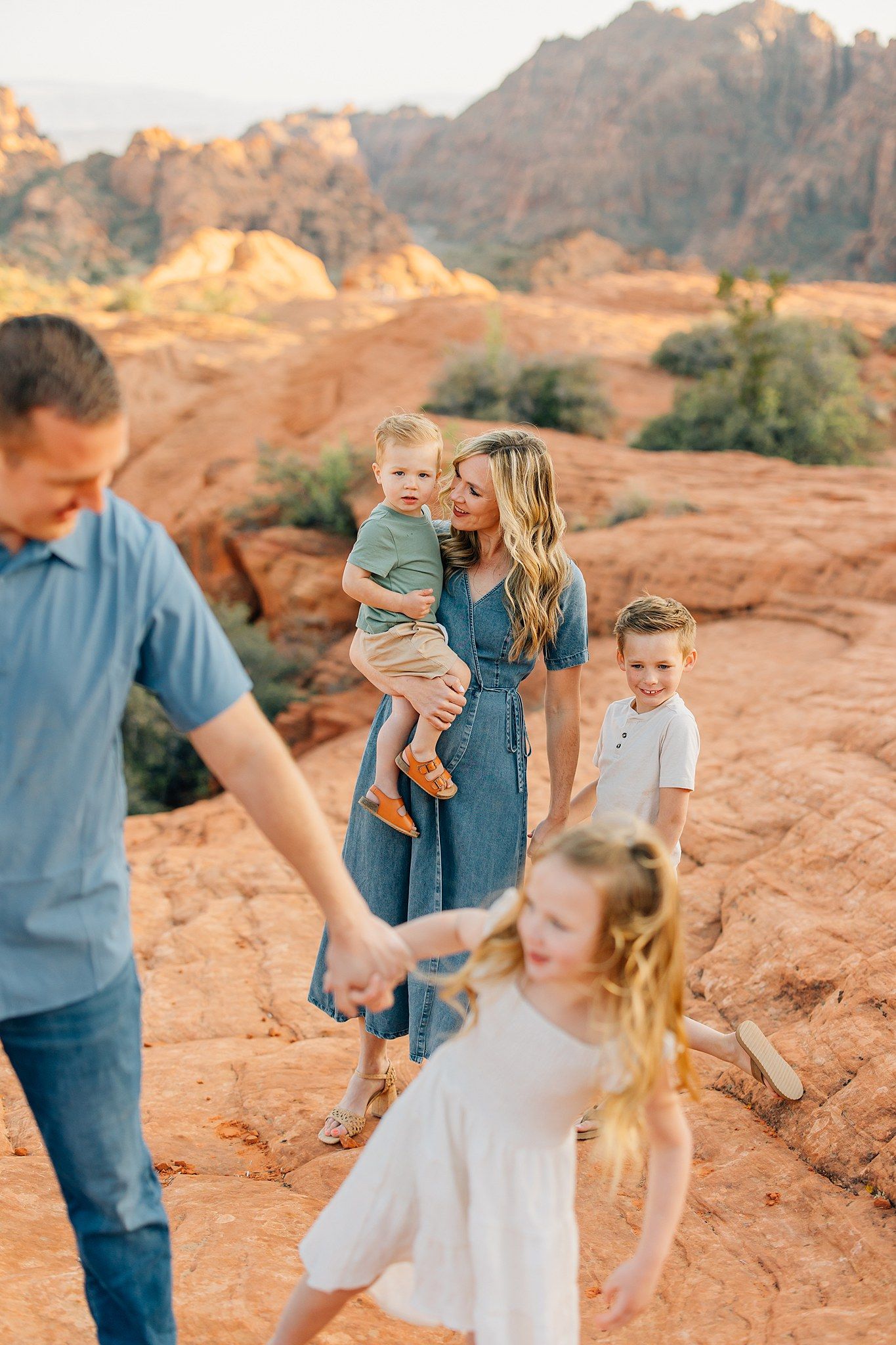 A family explores the red rock formations and desert landscape during golden hour at a scenic overlook.