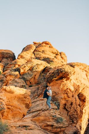 People climbing on dramatic orange sandstone formations against bright blue sky.