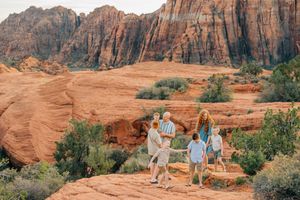 Family exploring red rock formations in Snow Canyon State Park with dramatic cliffs behind.