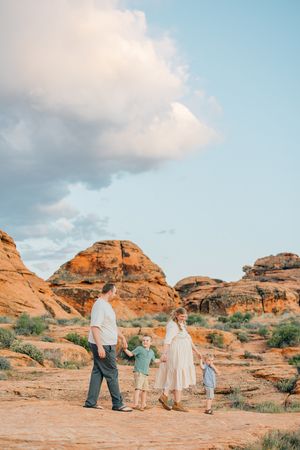 Family members walking together on red rock formations under blue sky with clouds.