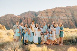 Large family group in light blue and white clothing poses in desert landscape at sunset.