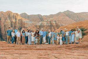 Large family group in coordinated blue outfits poses on red rock formations in desert setting.