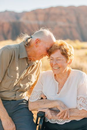 Elderly couple shares tender moment on bench against desert mountain backdrop.
