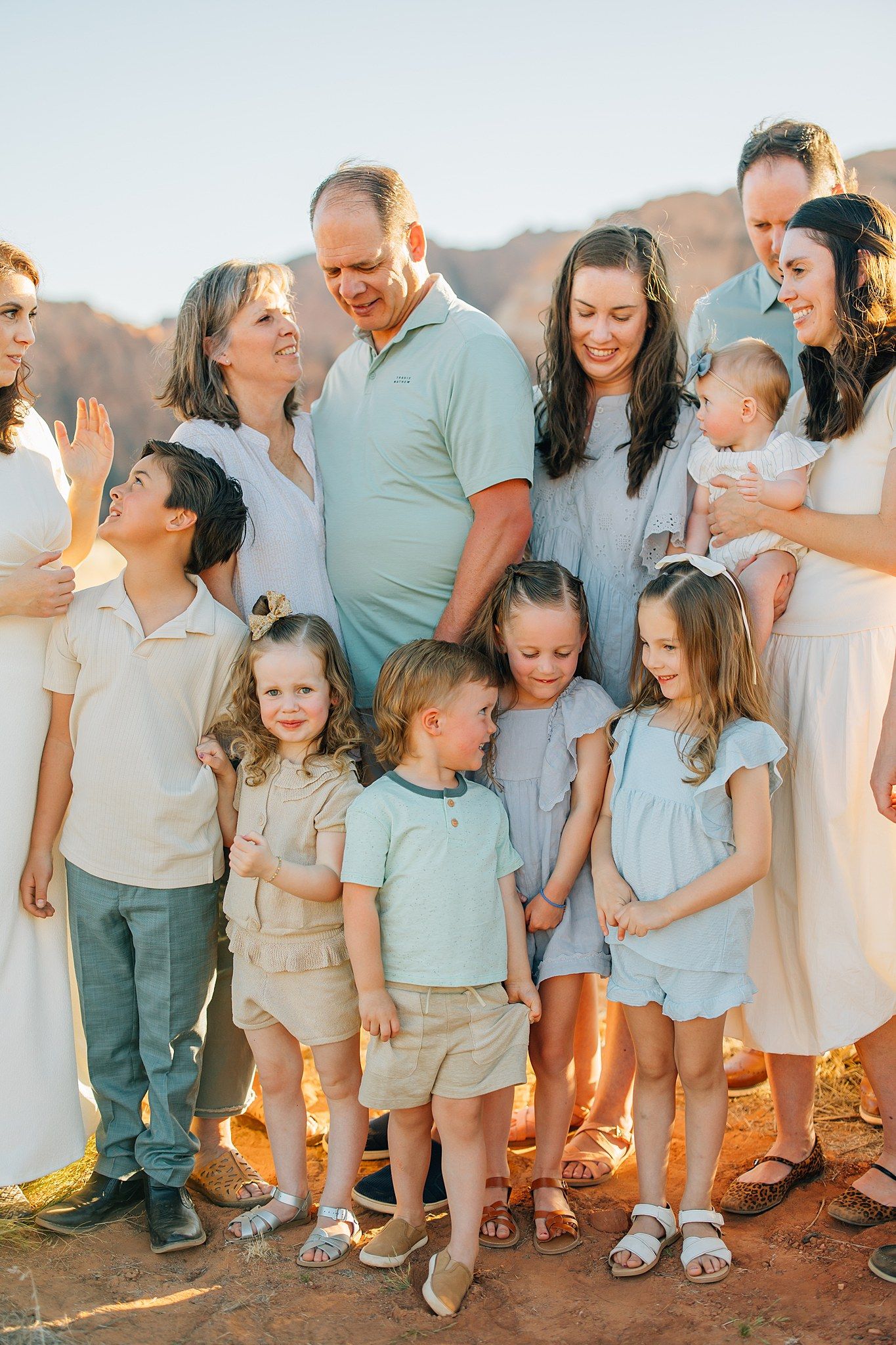 Extended family in coordinated pastel outfits laughs together against desert mountain backdrop.