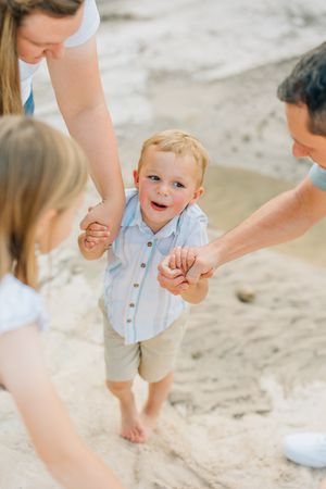 Toddler in light colored outfit plays joyfully on sandy ground.