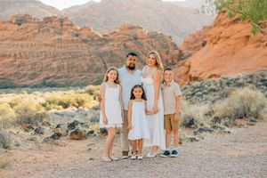A family poses together against a backdrop of red rock mountains and desert vegetation.