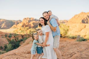 A family embraces while standing on red rocks during sunset in the desert.
