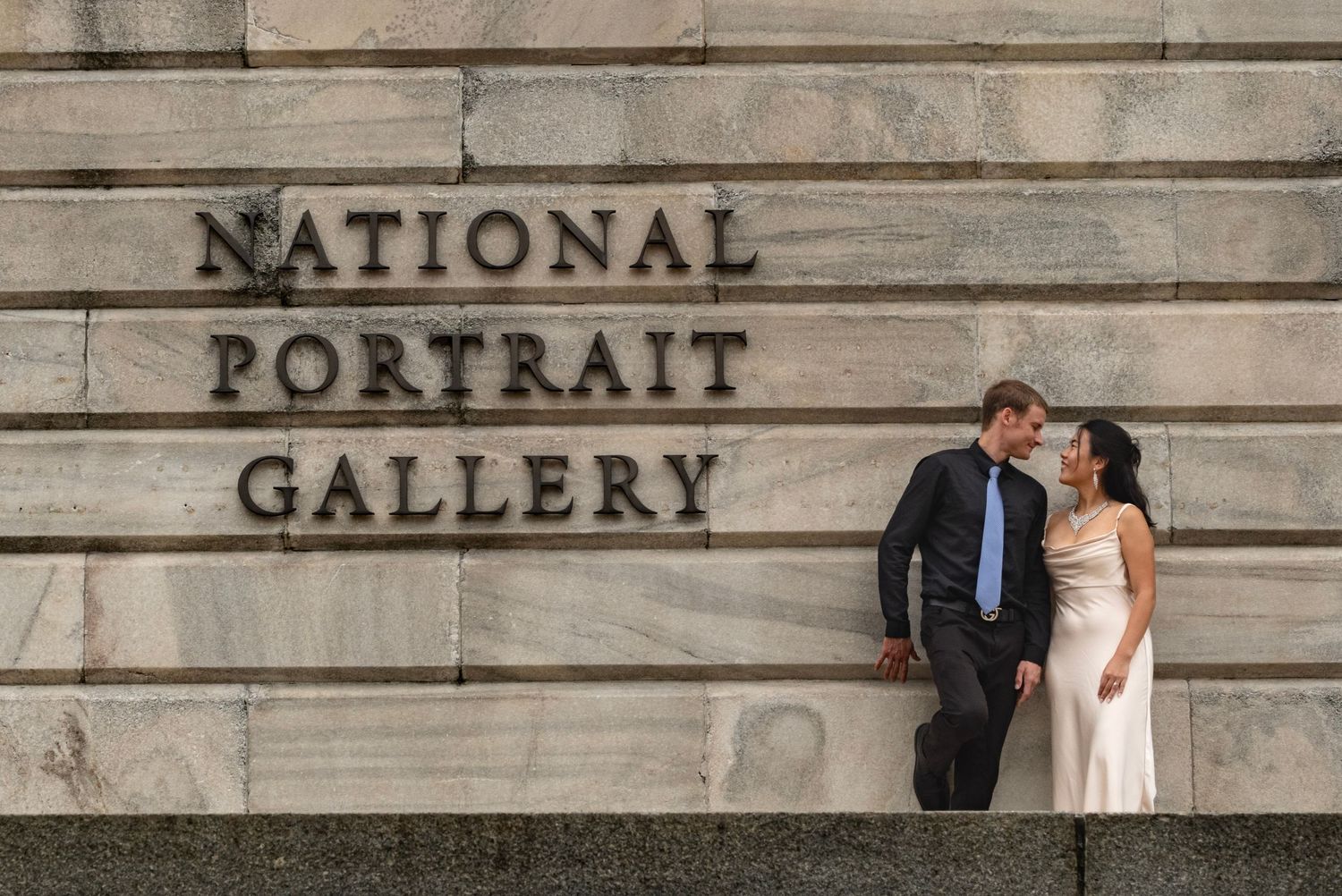 Elegant couple photographed against a stone wall with gallery signage.