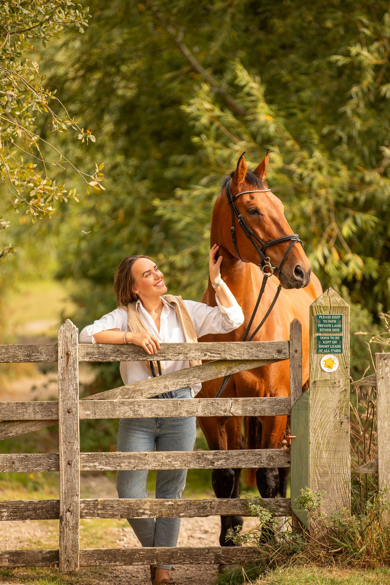 Young girl in denim overalls embraces a palomino horse in a sun-dappled forest setting.