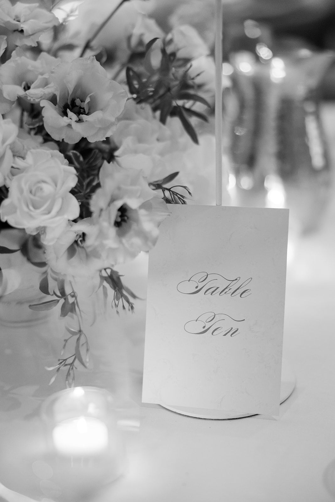 Black and white table number cards with elegant calligraphy displayed among floral centerpieces at a formal event.