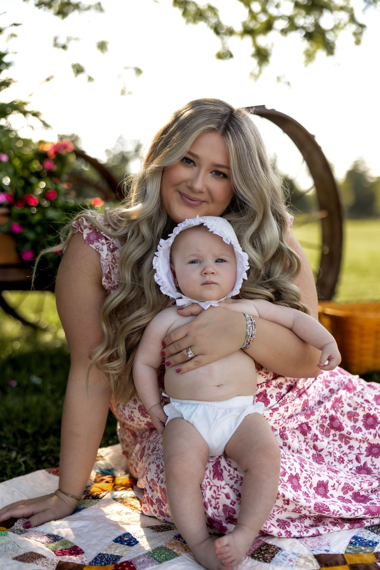 Mother and baby having a playful moment on a floral blanket during an outdoor summer photoshoot.