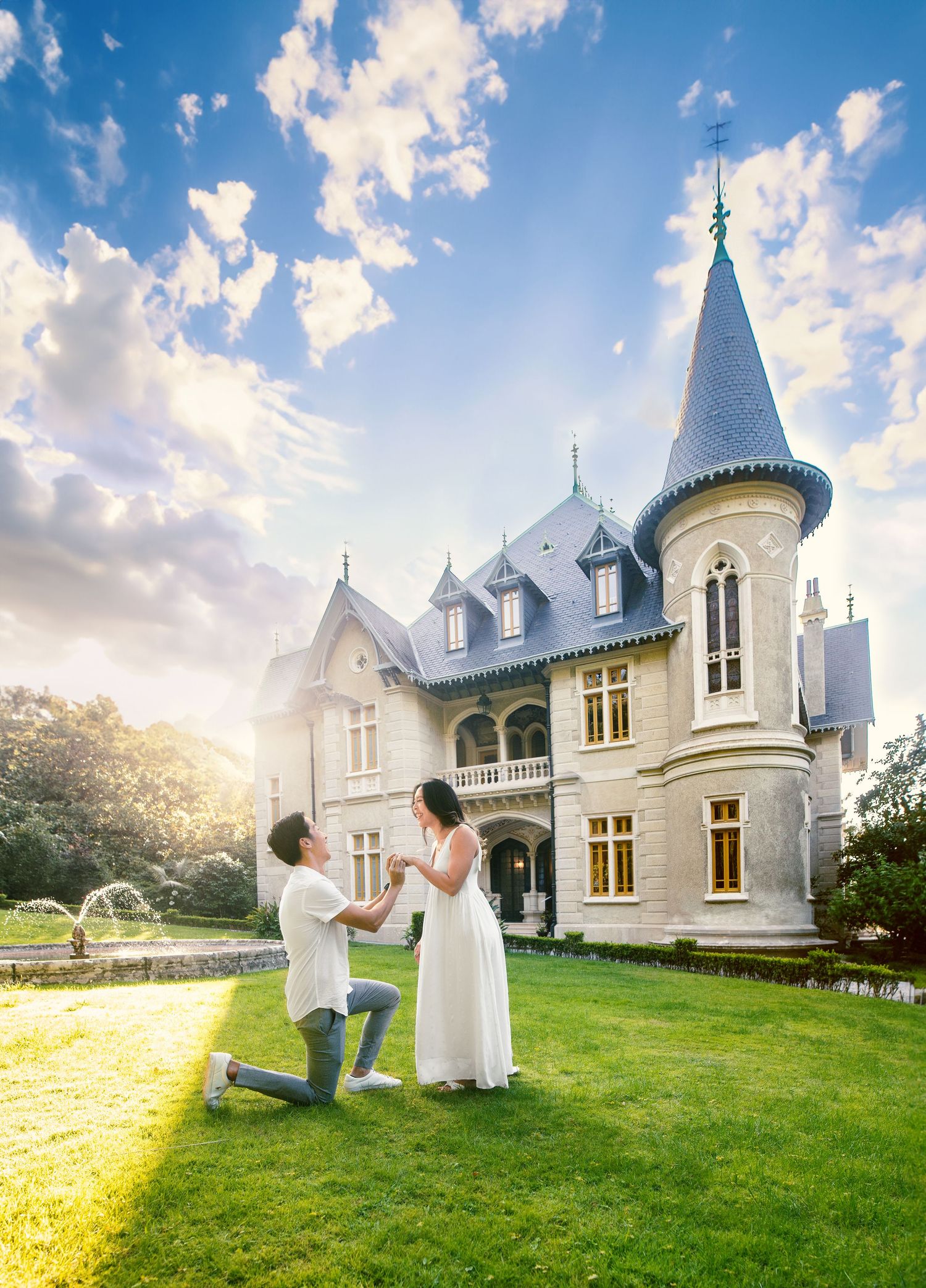 A romantic proposal scene unfolds on a sunny lawn in front of a beautiful white Gothic-style chateau with turrets and dormer windows.