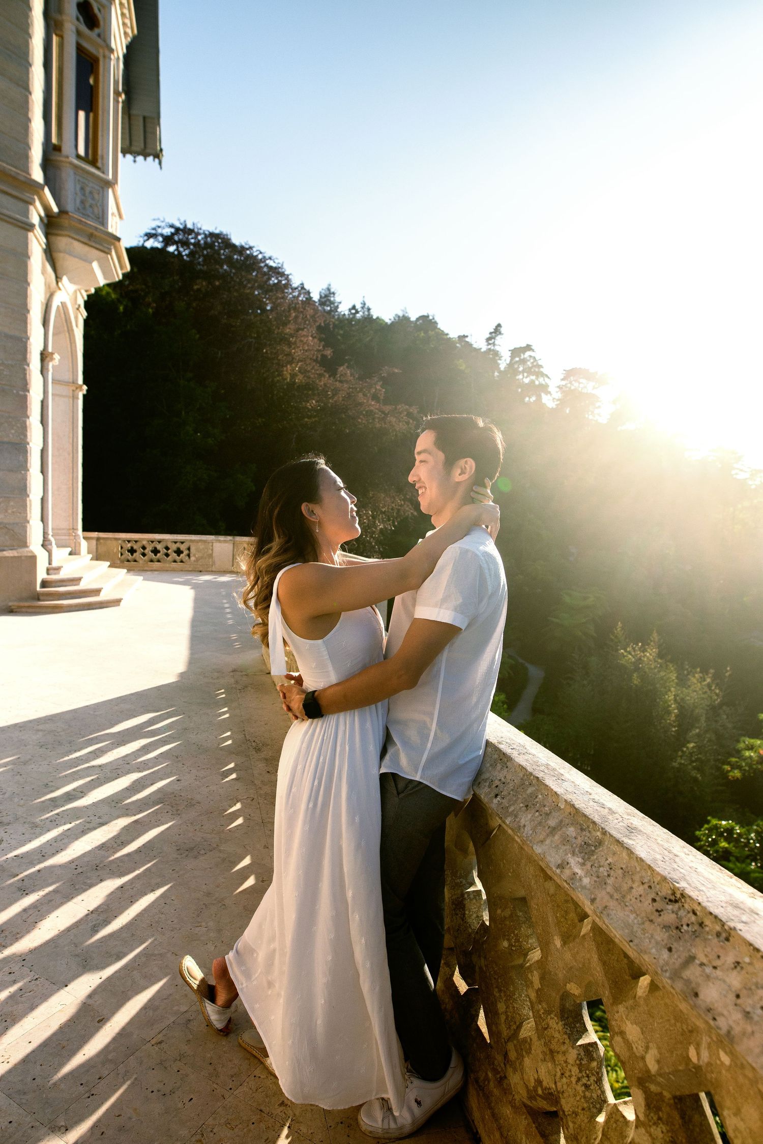 A couple embraces on a sunny terrace overlooking a scenic mountain landscape at golden hour.