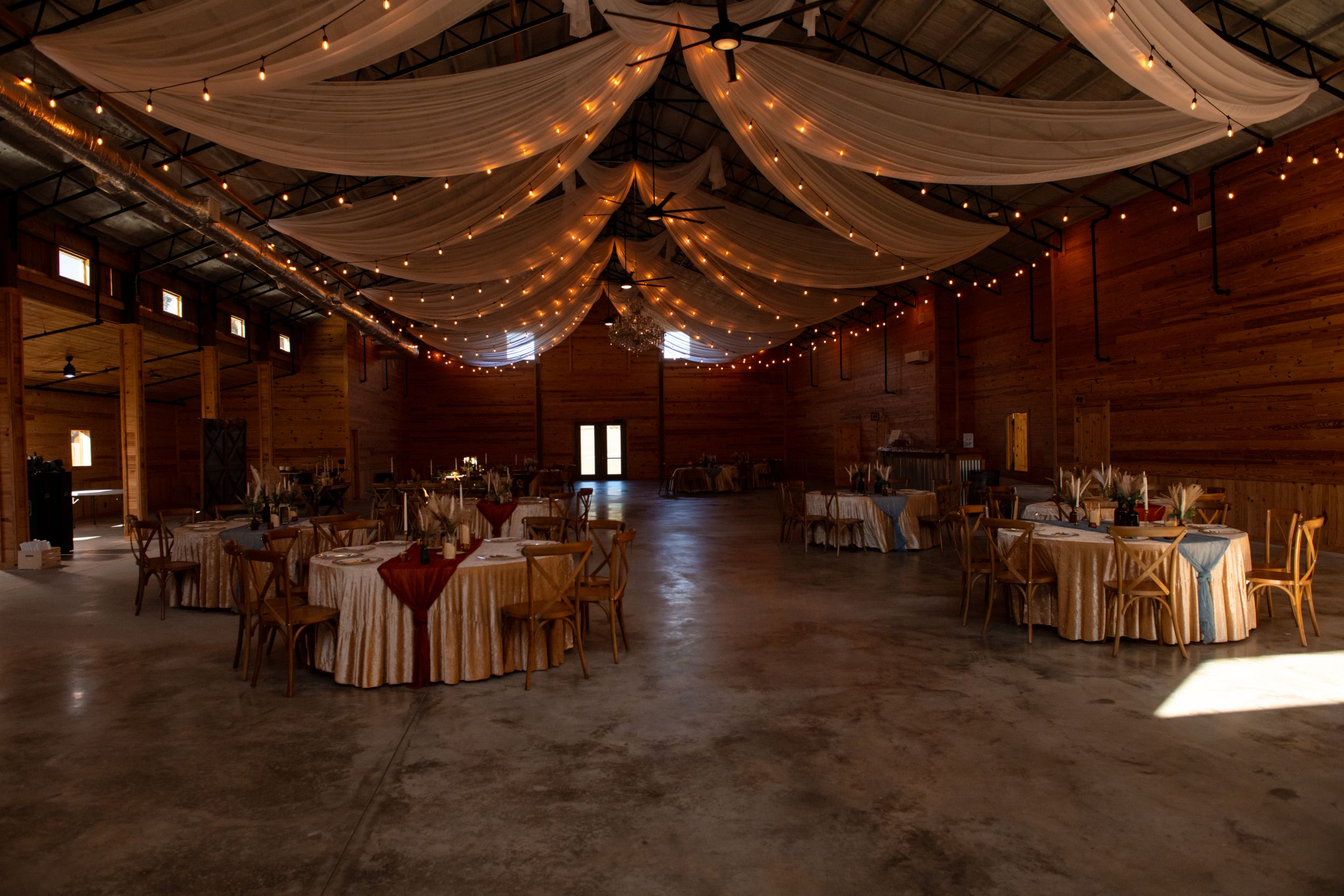 Rustic barn wedding venue interior with wooden beams and twinkling string lights creating a romantic atmosphere.