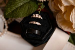 Close-up of wedding rings on green leaves and peach roses in a romantic wedding detail shot.