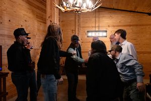 People gather inside a rustic wooden room with exposed timber walls and ceiling beams during a social event.