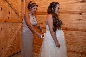 Mom help bride with her wedding gown. Mom and daughter emotional moment. Bride prepares in rustic wooden room for wedding ceremony.