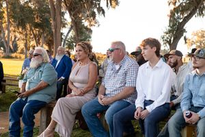 Guests seated outdoors on wooden benches during a sunset gathering.