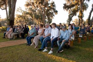 Wedding guests seated outdoors under moss-draped oak trees during sunset ceremony.