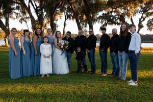 Wedding party stands together on a grassy lawn at sunset with Spanish moss draped trees in the background.
