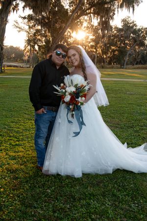 A couple poses together on a grassy field during golden hour with Spanish moss hanging from trees in the background.