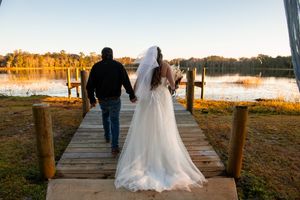 Couple walking along wooden dock at sunset with water and trees in background. Lake.
