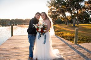 Wedding celebration on a wooden dock during golden hour with water and trees in background.