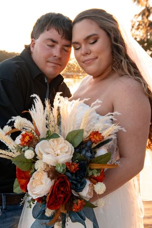 Newlyweds embrace during golden hour with a stunning bouquet of red and white flowers.