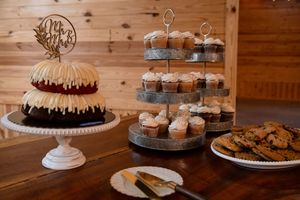Wedding dessert display featuring cupcakes and cakes on tiered stands with rustic wooden backdrop.