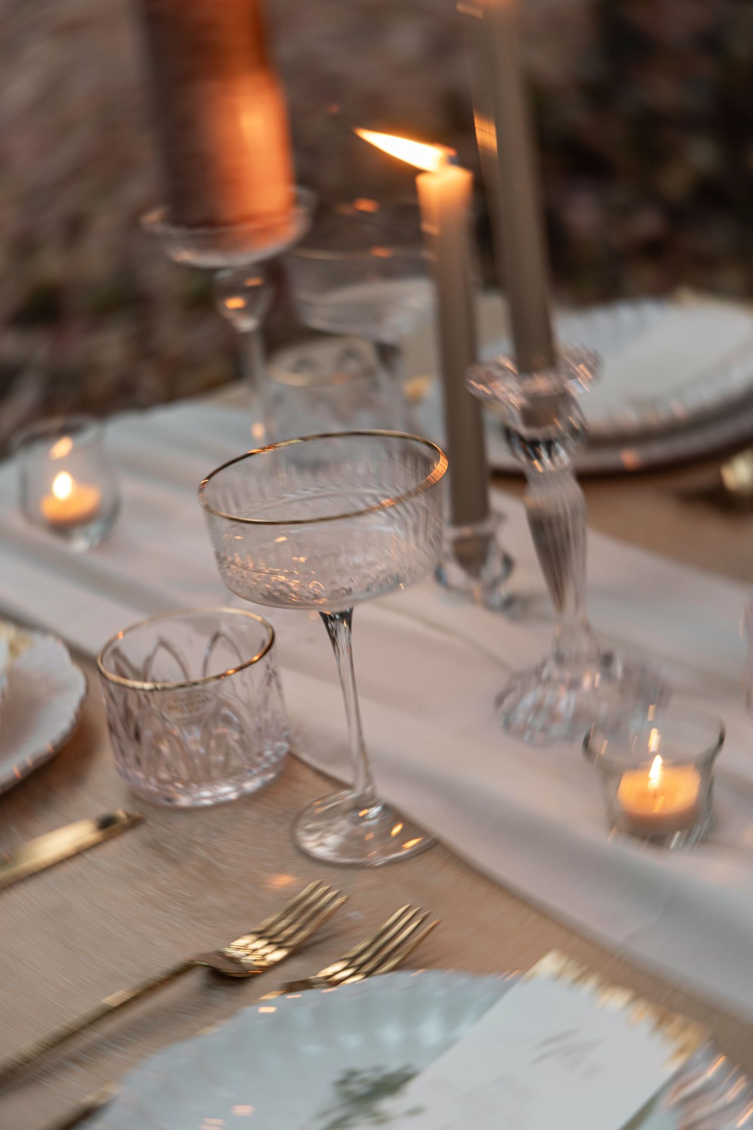 Elegant table setting with crystal glasses, white linens, and glowing candlelight creating a romantic dining atmosphere.