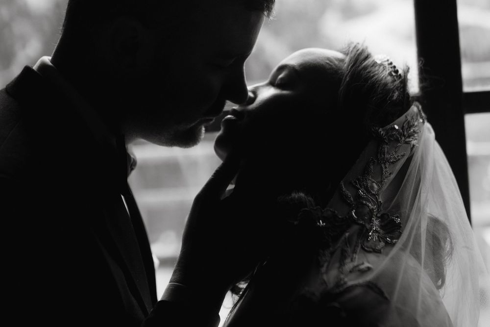 Black and white wedding photo of bride and groom sharing an intimate moment, bride wearing veil and floral headpiece.