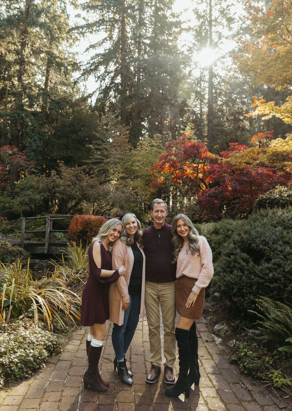A group stands together on a brick path surrounded by vibrant fall foliage and evergreen trees in a garden setting.