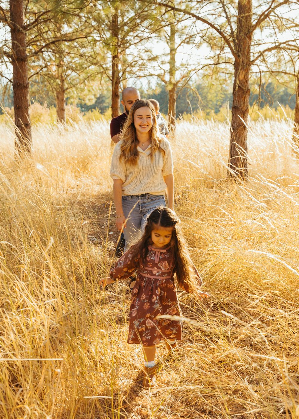 People playing and running through tall golden grass in a sunlit forest during sunset creating a dreamy atmosphere.