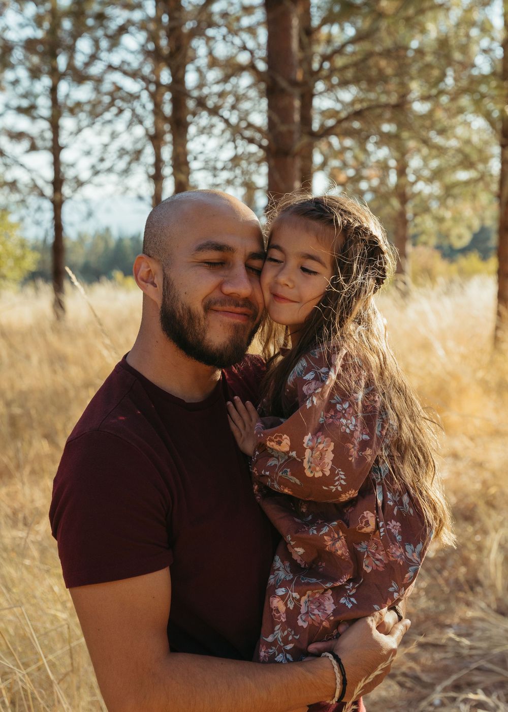 A loving couple shares tender moments together in a natural outdoor setting with pine trees and golden grass.