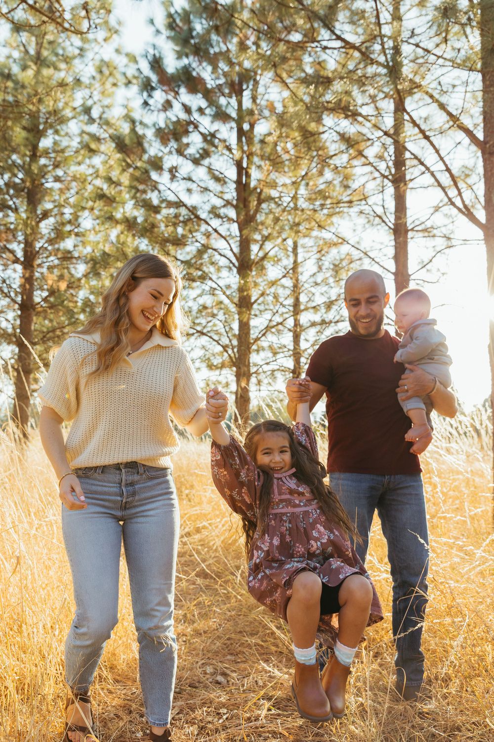 Family enjoys playful moments together in a sun-lit pine forest during golden hour.